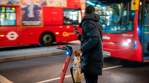 Man in London, UK in traffic on an electric scooter waiting to cross the road with double decker buses in the background