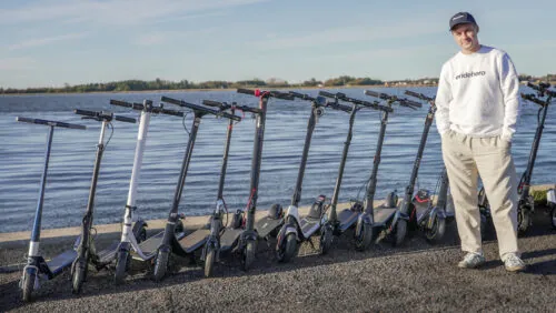 Rasmus from ERideHero next to a wide range of entry-level electric scooters with the ocean in the background