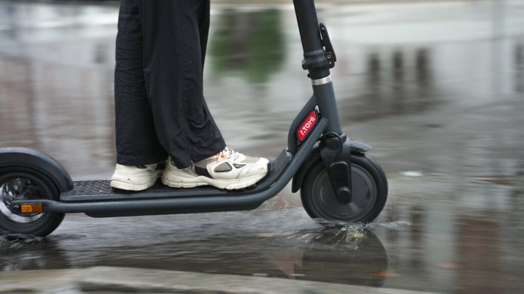 Close-up of an electric scooter riding through a water puddle with water splashing up