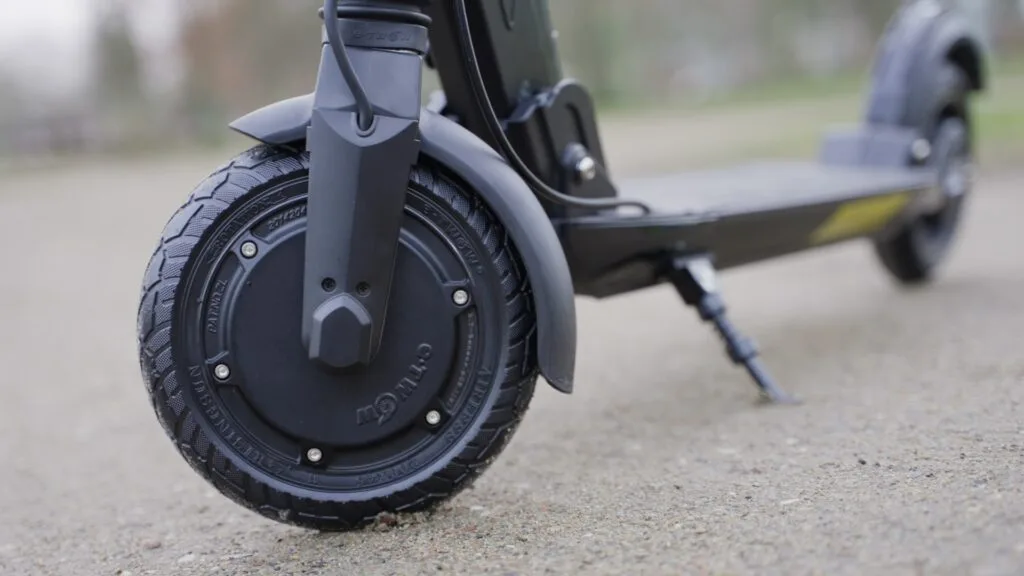 Close-up of the Fluid Mosquito electric scooter's front wheel and motor, highlighting the tread pattern on a textured pavement