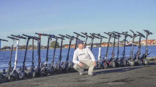 Rasmus from ERideHero sitting at the shore in front of a wide selection of more than 20 electric scooters